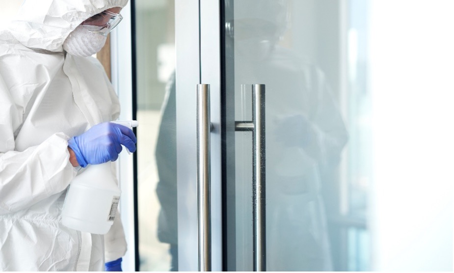 Alt text: Corporate Hygiene cleaning professional in PPE disinfecting glass door